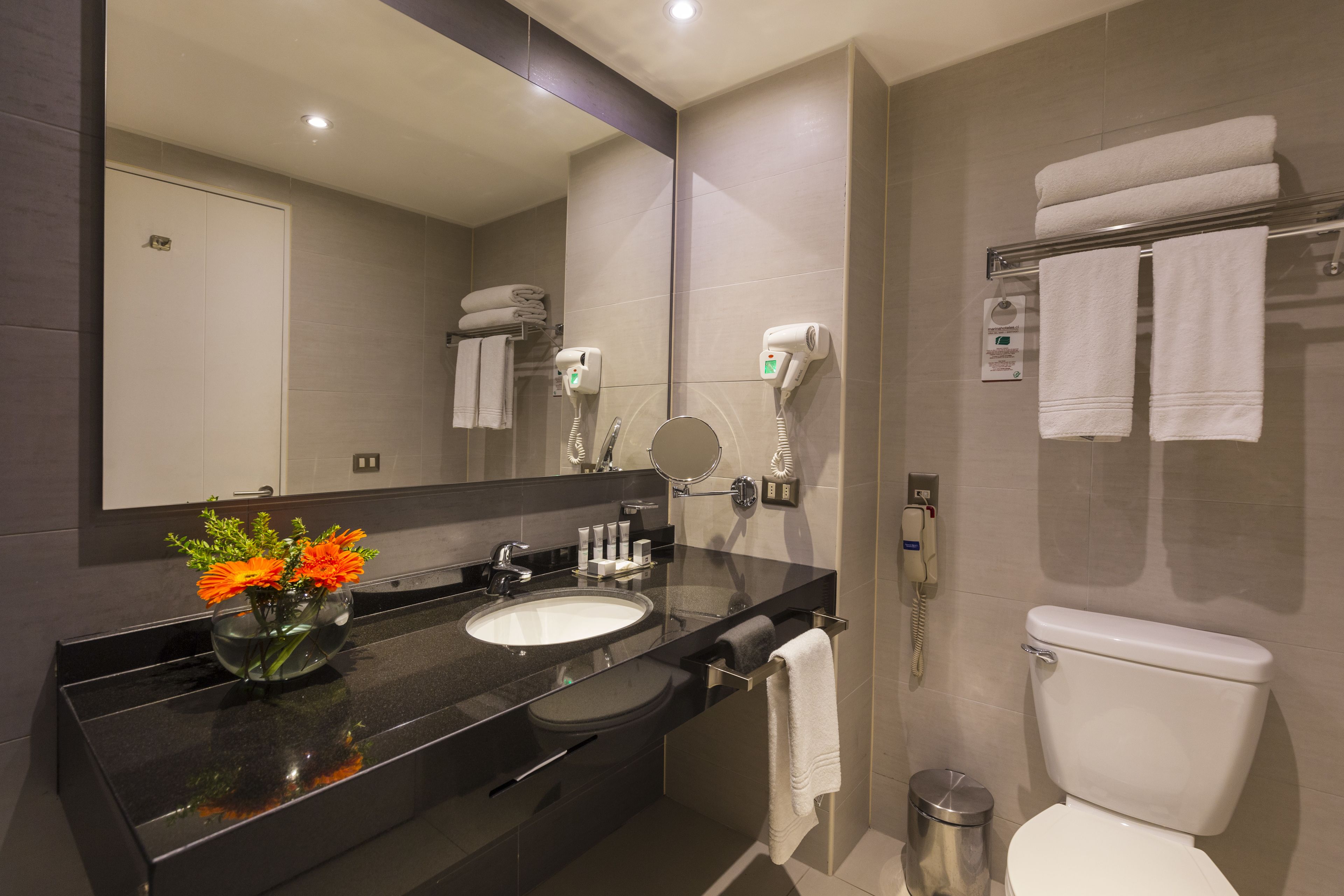 Uma casa de banho moderna com lavatório de bancada preta, espelho, sanita e porta-toalhas.