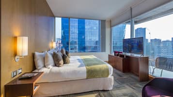 Une chambre d’hôtel moderne dotée d’un grand lit, d’une télévision, d’un bureau et offrant une vue sur la ville grâce à de grandes fenêtres.