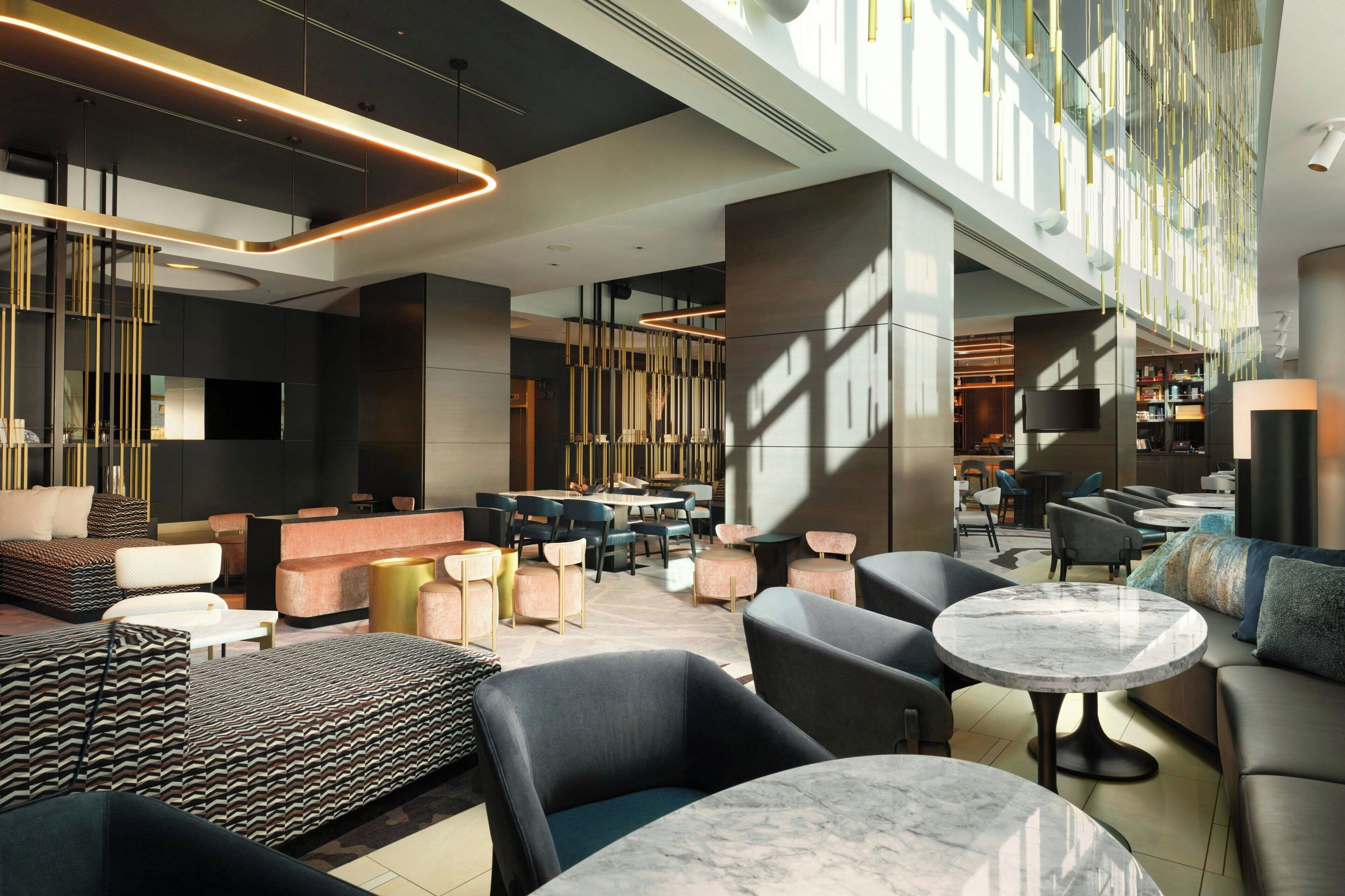 A modern hotel lobby with a spacious seating area, a bar, and a large TV screen.