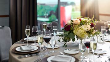 A dining table set for a meal with wine glasses, plates, and a centerpiece of flowers.