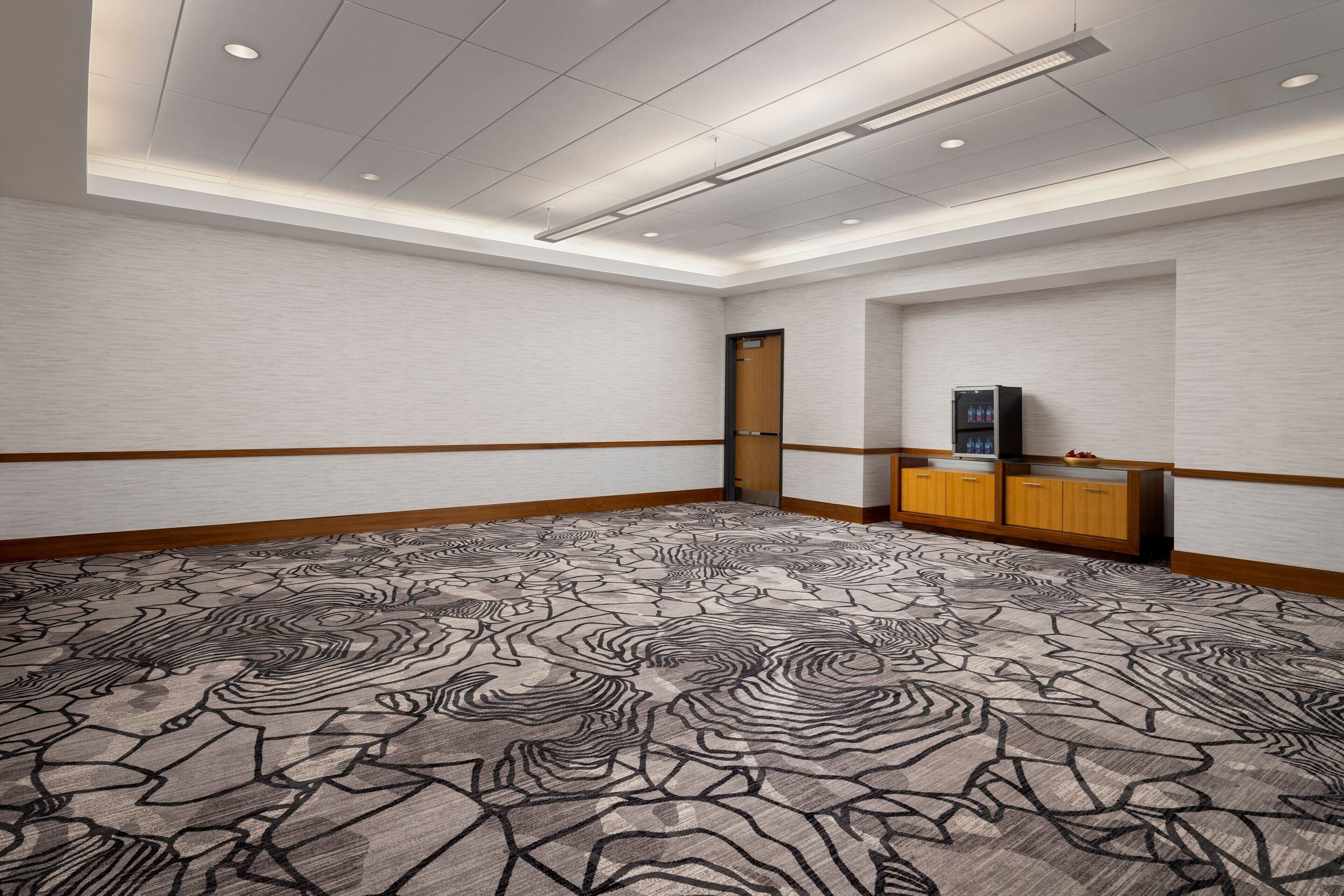 A conference room with a patterned carpet, wooden paneling, a wooden cabinet with a television, and a door.