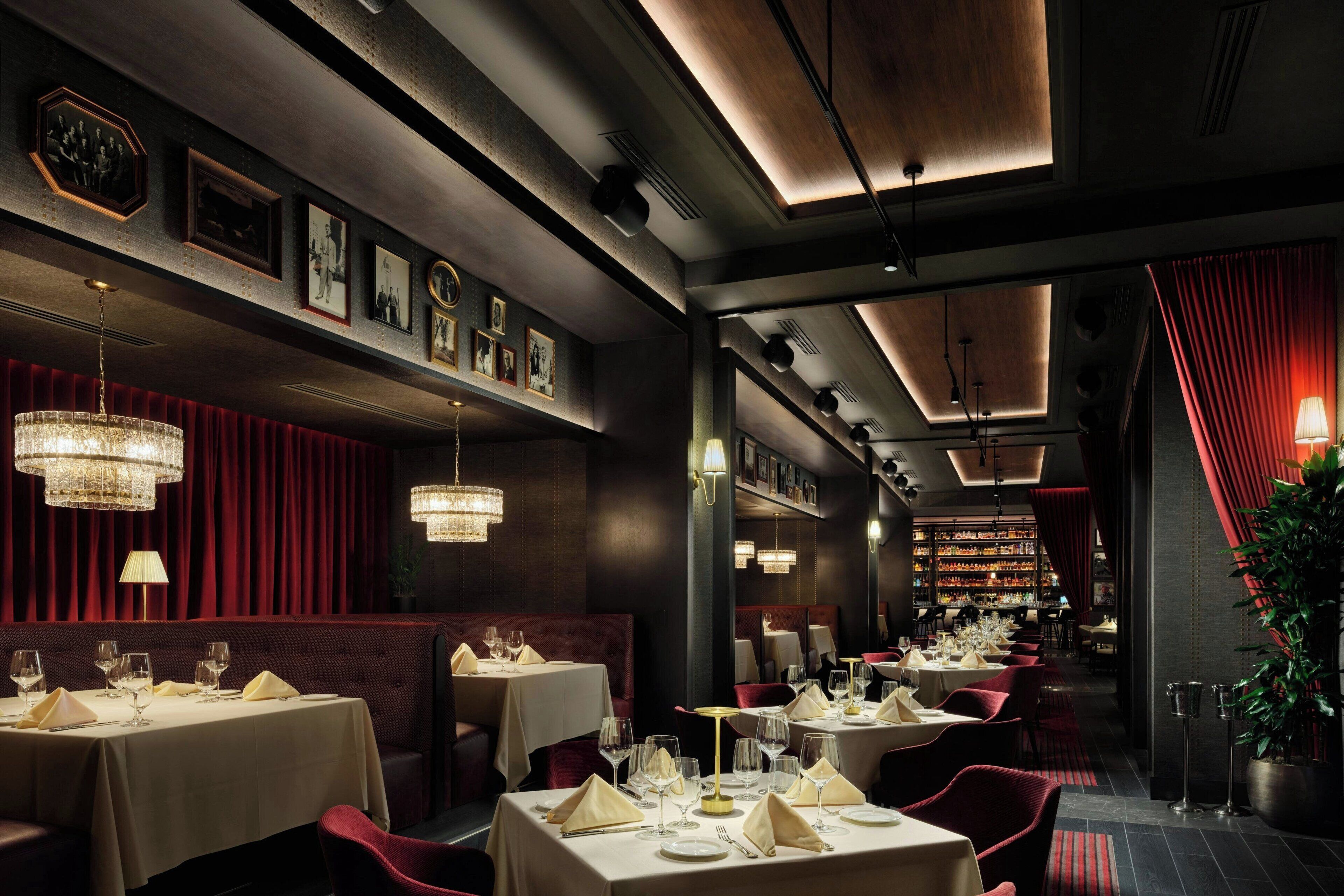 A restaurant with tables set for dining, a bar area, and a red curtain backdrop.