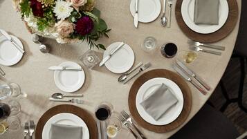 Ein runder Tisch ist für eine Mahlzeit gedeckt, mit Tellern, Besteck und Gläsern, umgeben von einem floralen Mittelstück.