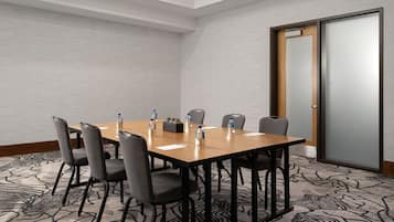 A conference room with a wooden table, grey chairs, water bottles, and a patterned carpet.