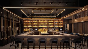 A modern bar area with a long counter, multiple bar stools, and shelves stocked with bottles. - JW Marriott Indianapolis (Indianapolis)