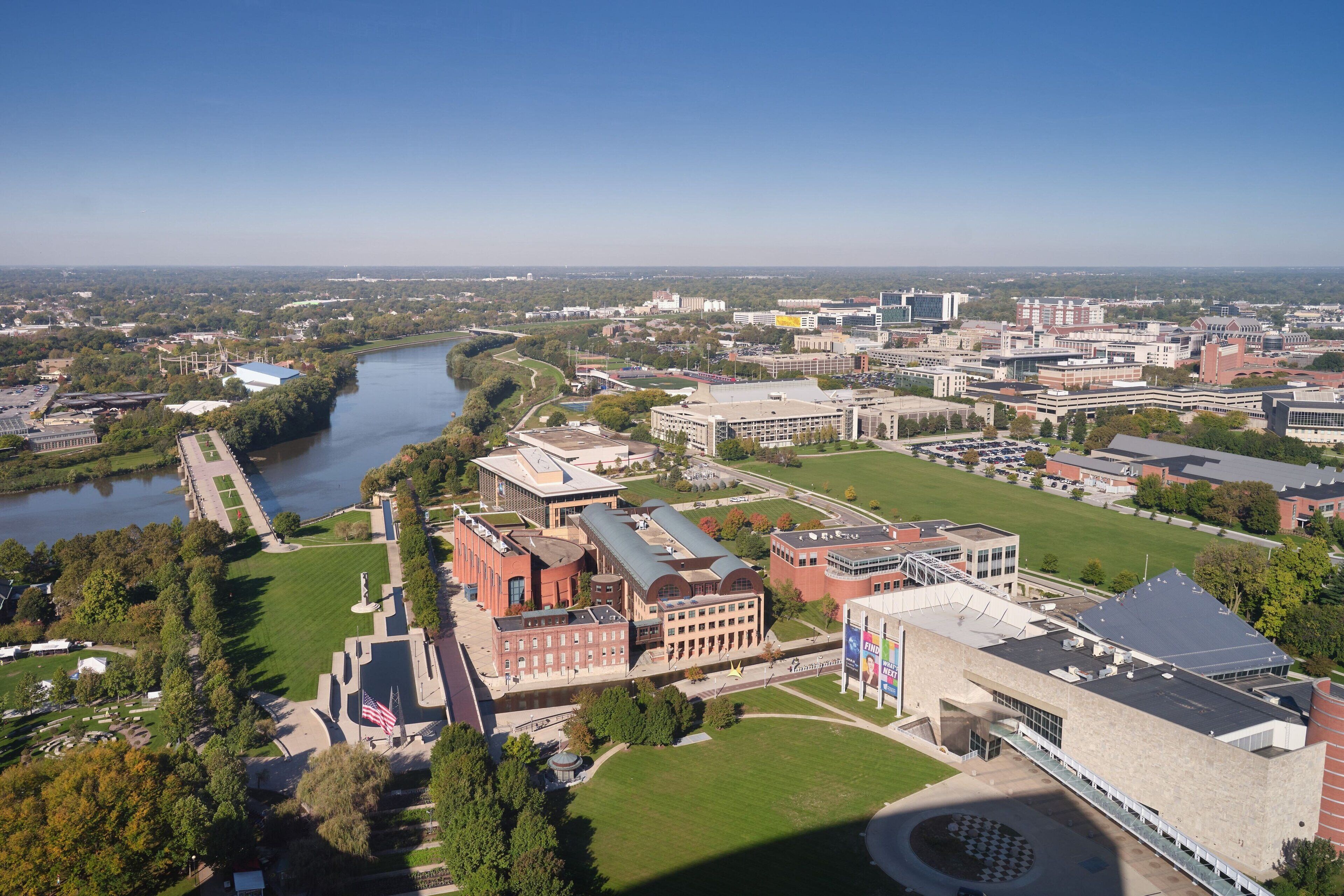 An aerial view of a campus with buildings, a river, and green spaces.