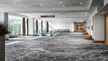 A hotel lobby with a patterned carpet, seating areas, and a staircase leading to another floor.