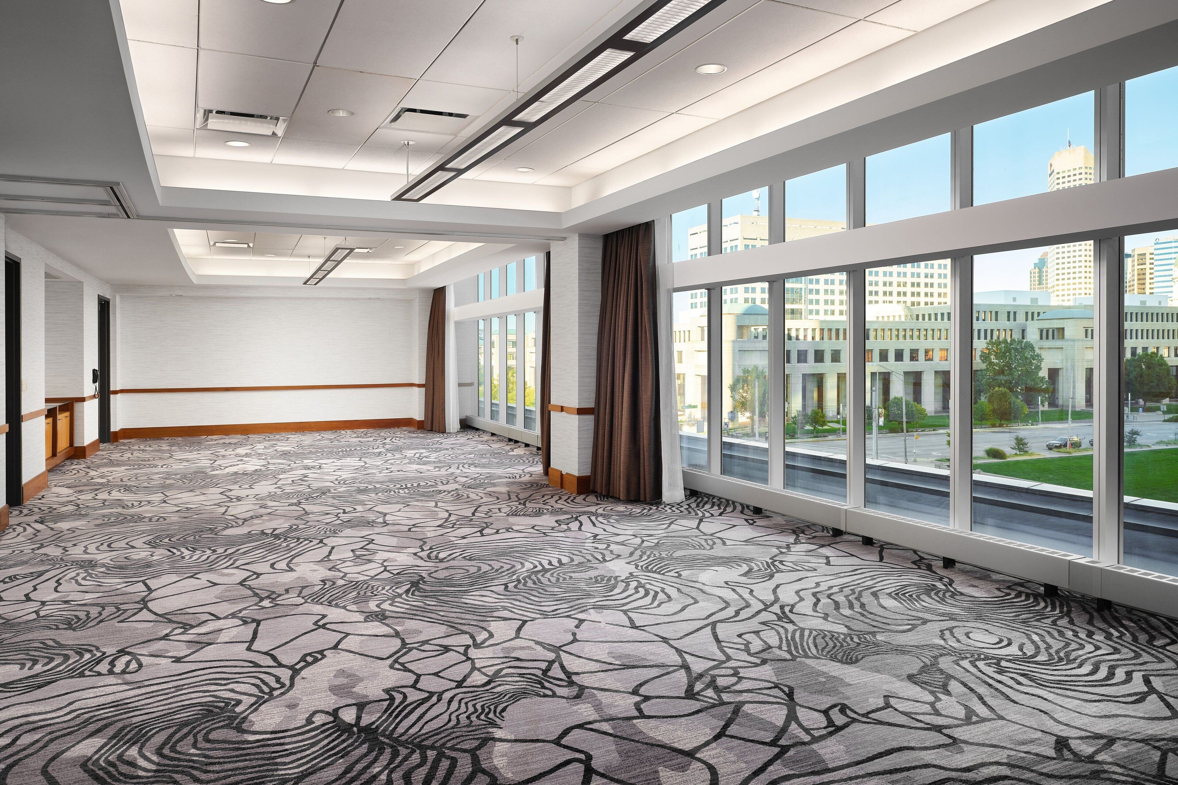 Uma sala de conferências espaçosa com carpete estampado, grandes janelas com cortinas e vista para edifícios da cidade.