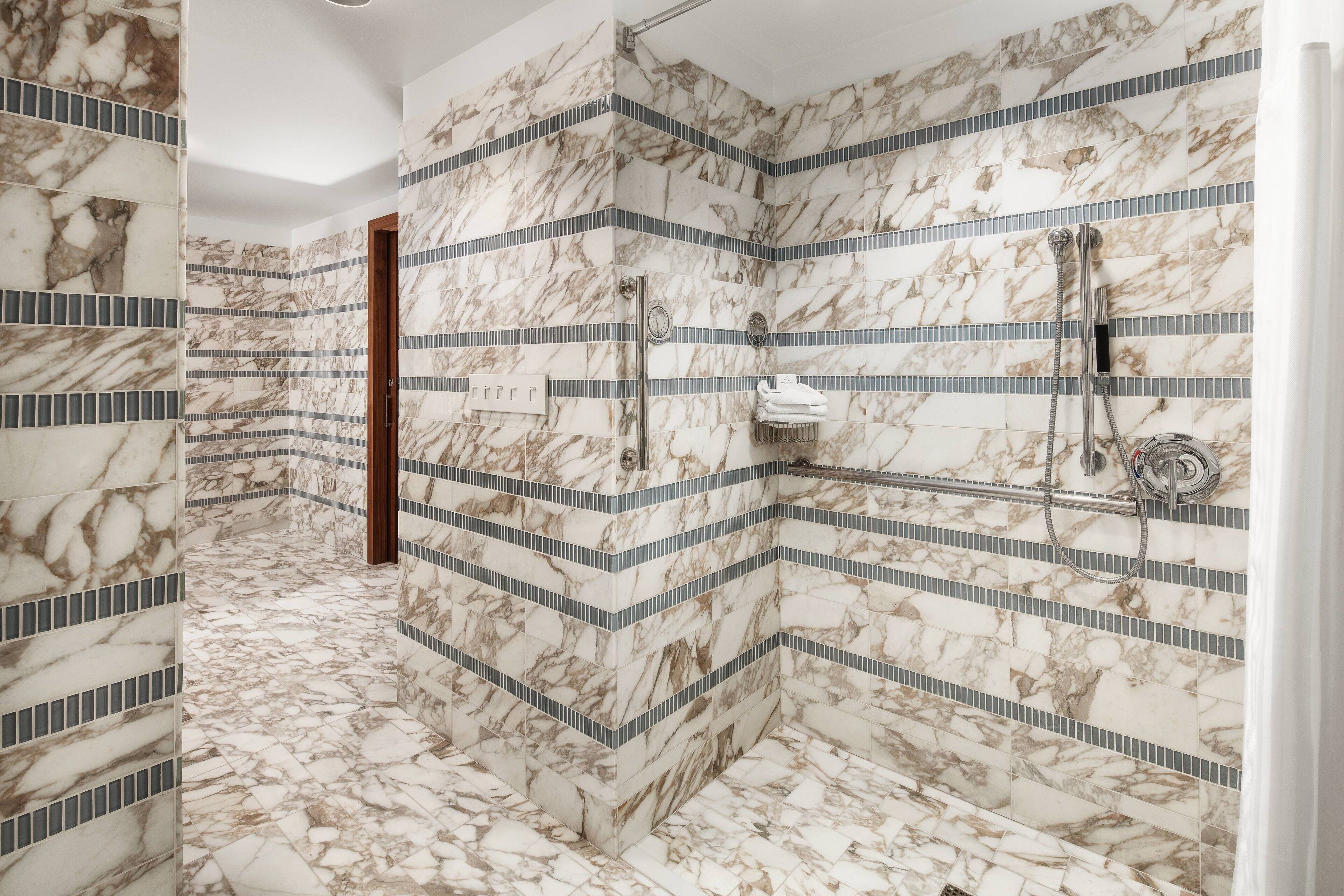 Ein modernes Badezimmer mit Marmorwänden und -boden, einer Dusche mit mehreren Armaturen und einer Holztür.