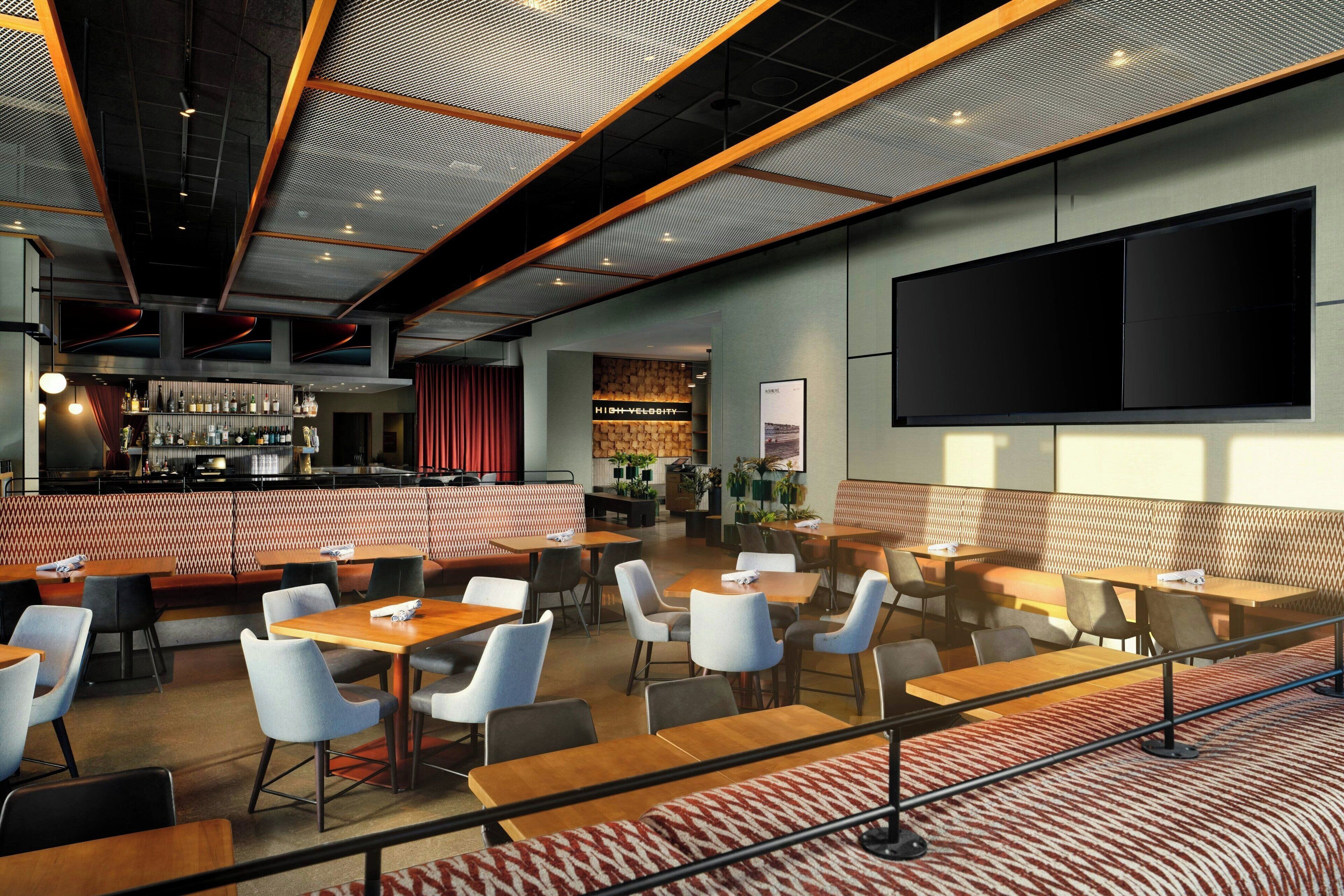 Un restaurante moderno con zona de bar, mesas y una pantalla grande para presentaciones.
