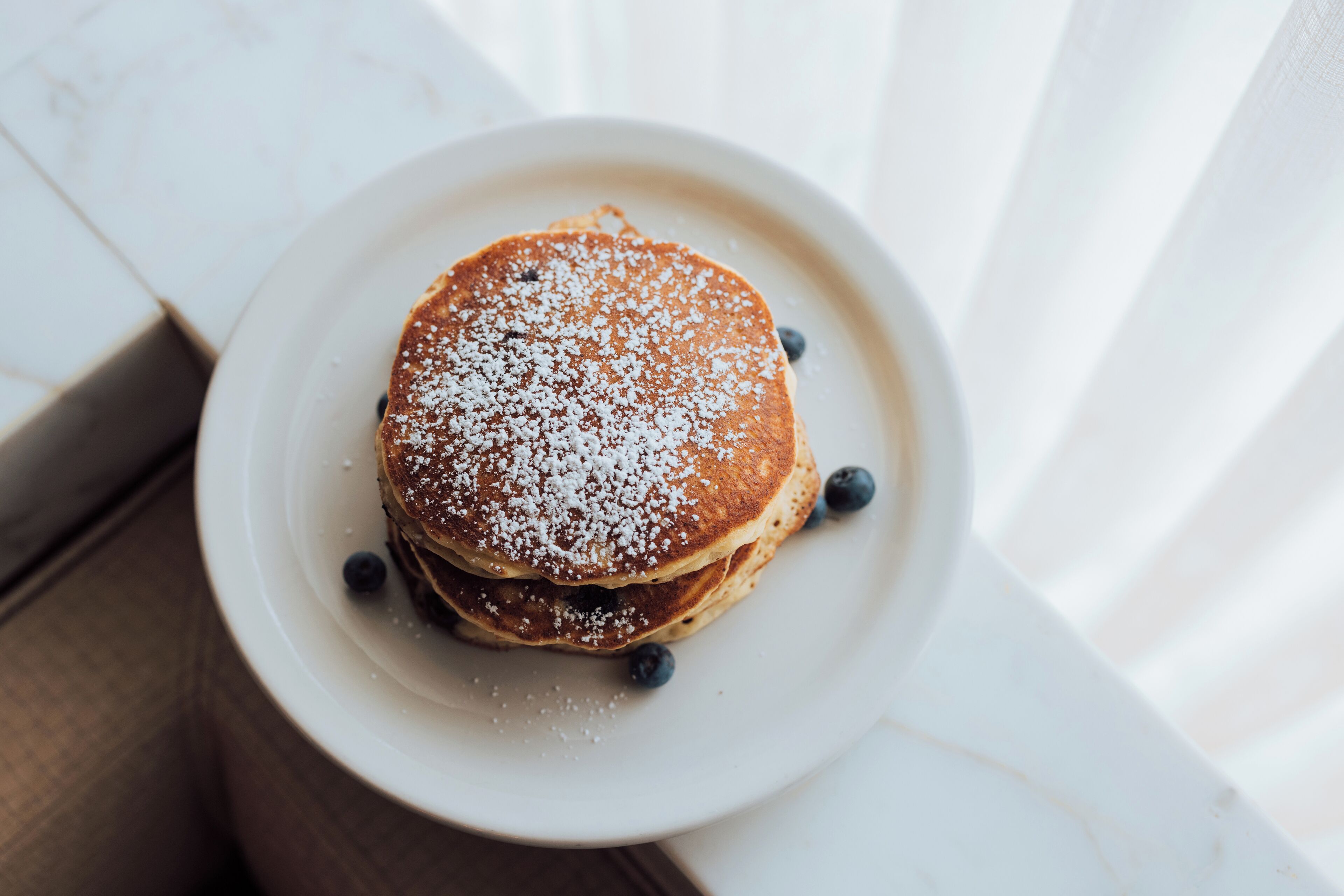 A stack of pancakes on a white plate with powdered sugar and blueberries.