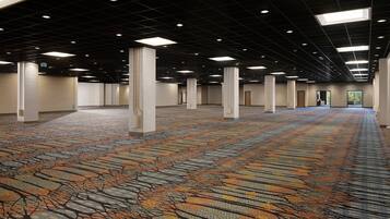 A spacious indoor area with a patterned carpet, multiple columns, and a grid of ceiling lights.