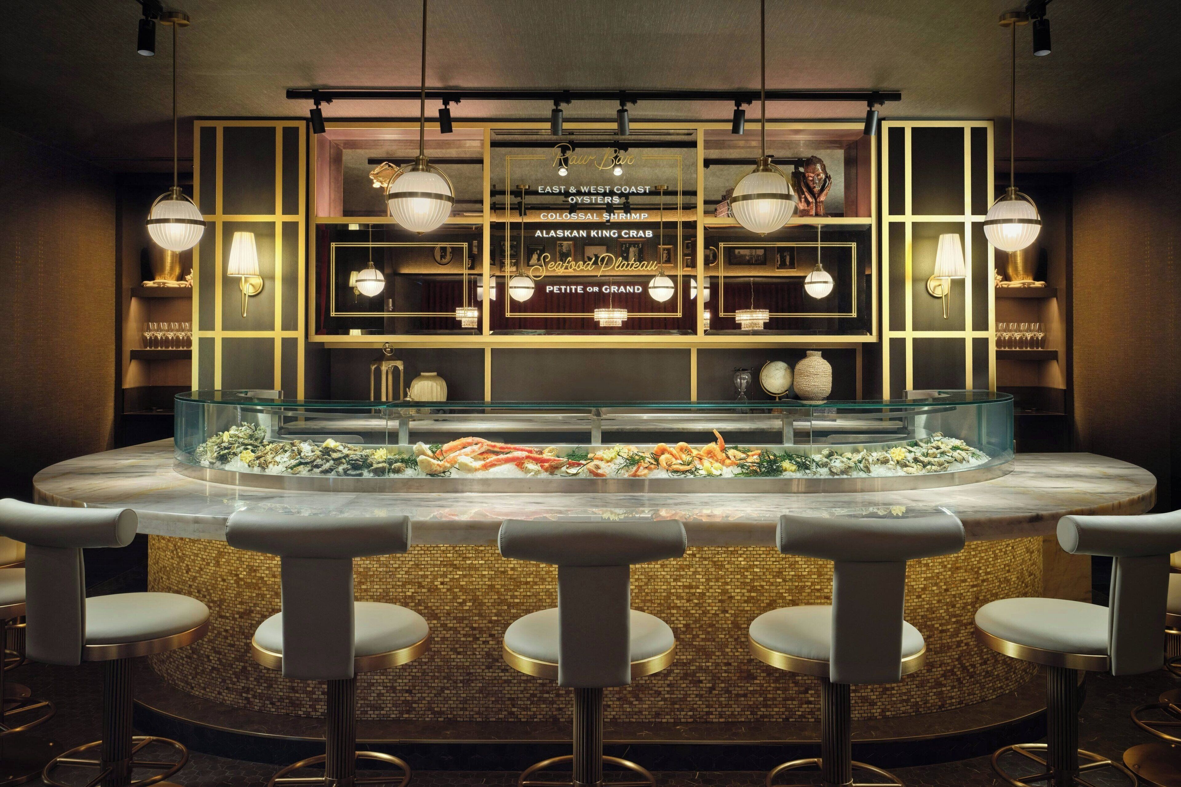 Un bar à fruits de mer doté d'une vitrine réfrigérée où sont exposés différents produits de la mer, de tabourets de bar et d'un éclairage suspendu.