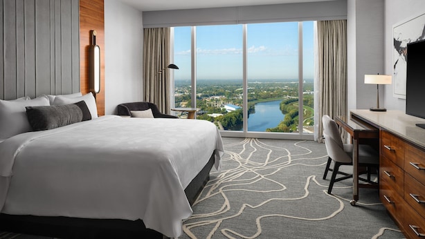 A hotel room with a large bed, a desk, a chair, a TV, and a view of a cityscape and river. - JW Marriott Indianapolis (Indianapolis)