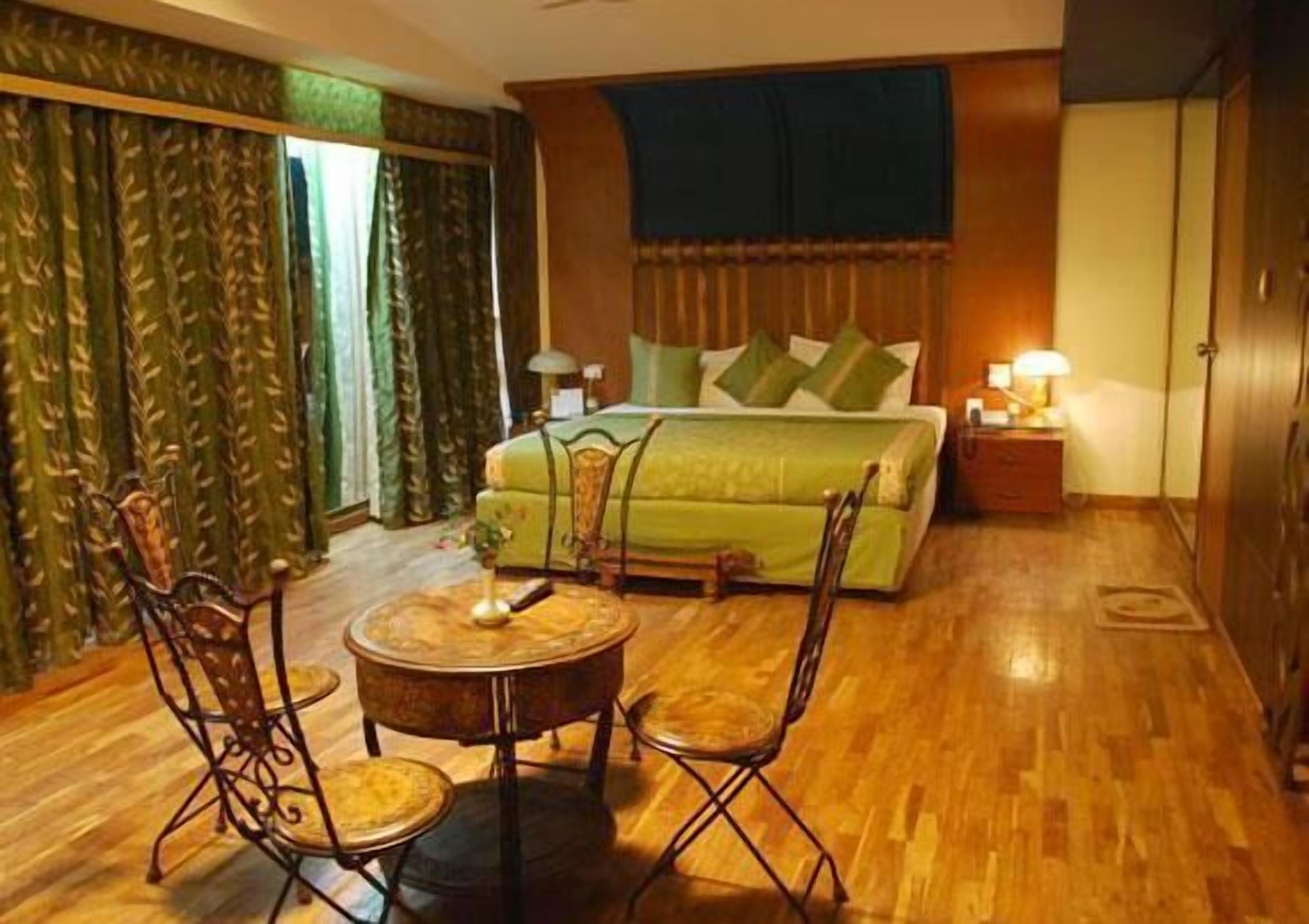 A hotel room with a bed, two chairs, a small table, and a nightstand with a lamp.