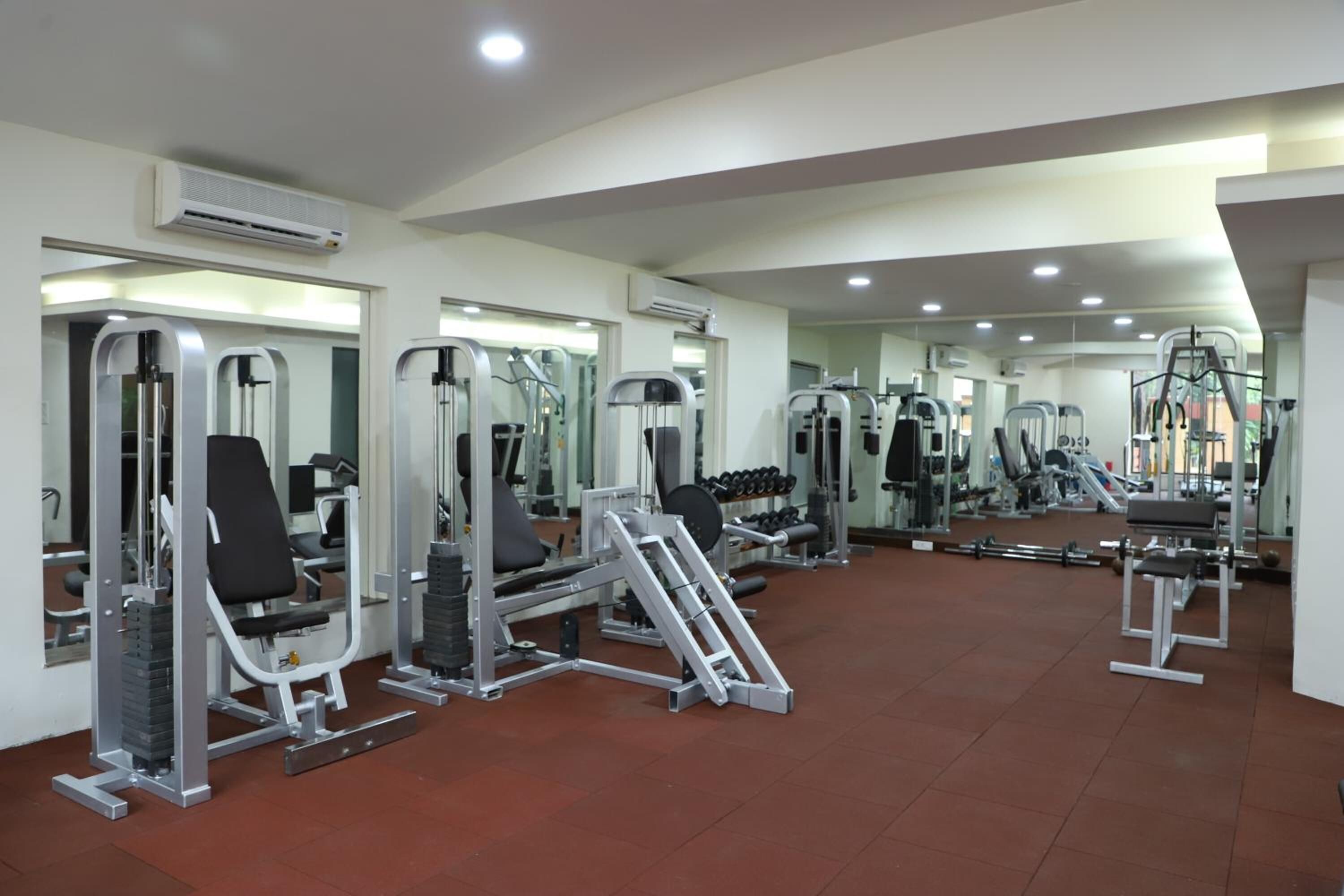 Un gimnasio con diversas máquinas de ejercicio, espejos y suelo de baldosas.