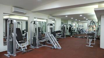 Un gimnasio con diversas máquinas de ejercicio, espejos y suelo de baldosas.