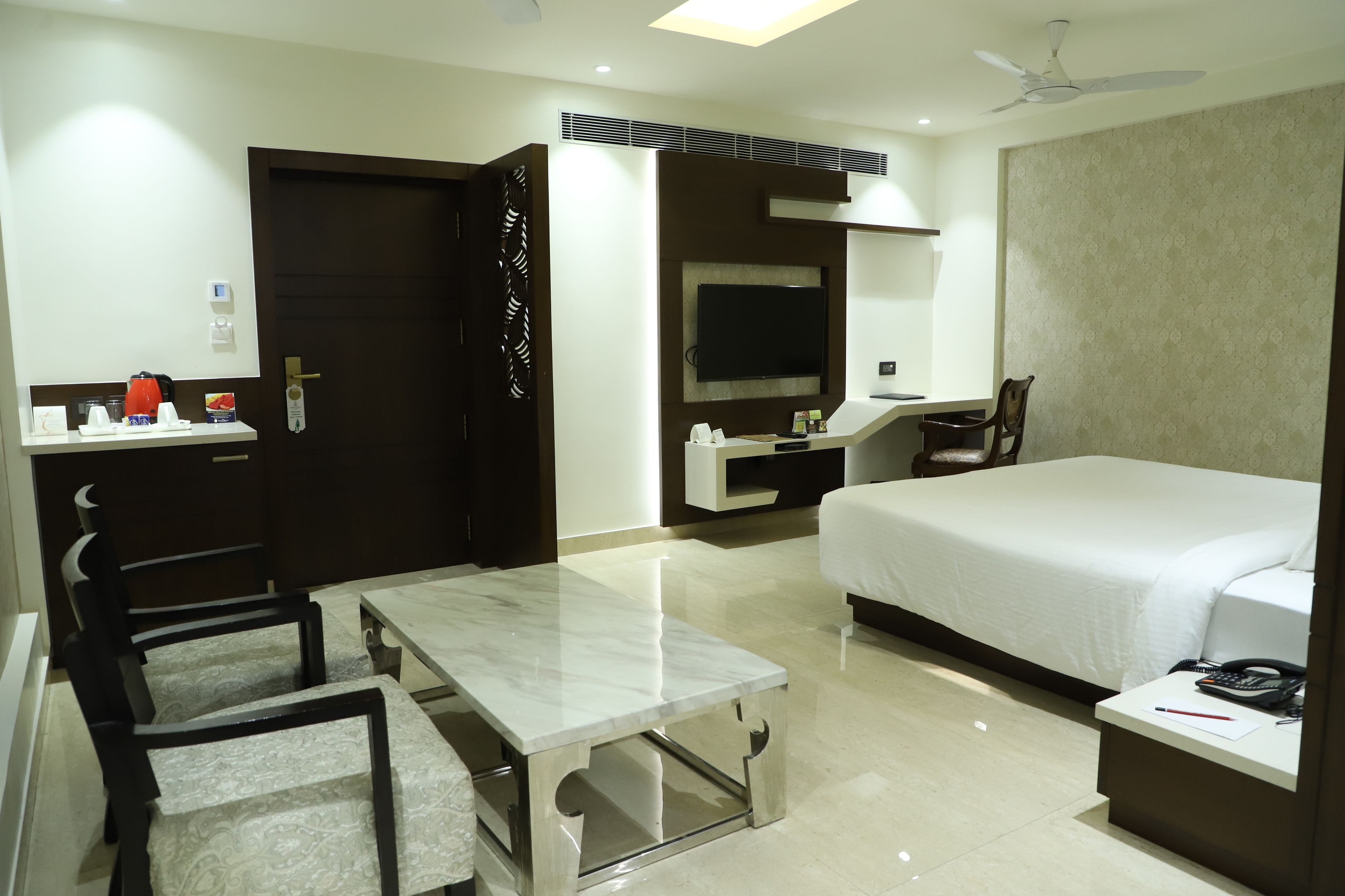 A hotel room with a bed, a desk, a chair, a TV, and a ceiling fan.