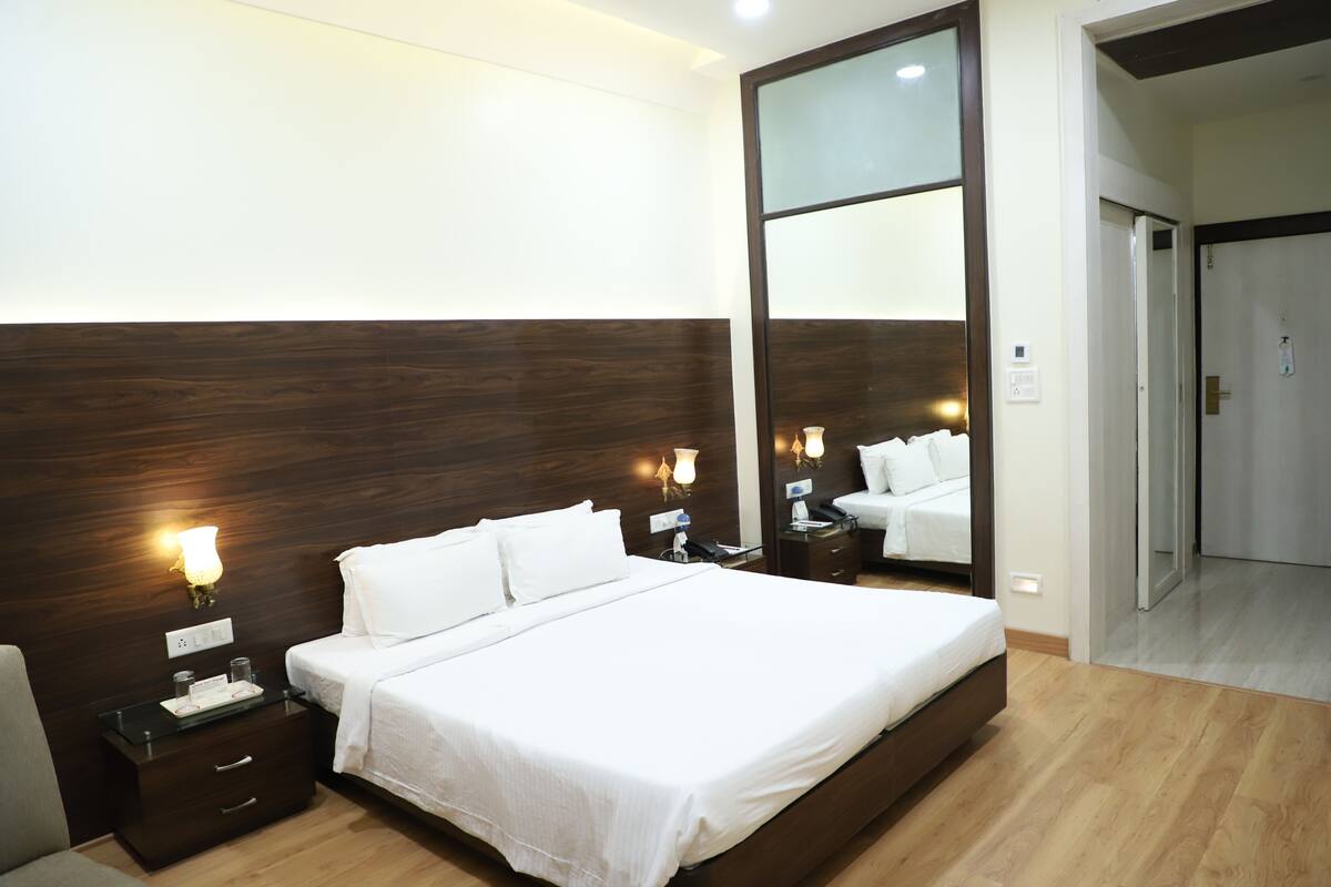 A hotel room with a large bed, a nightstand, a mirror, and a door leading to another room.