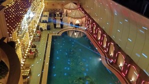 Un área de piscina interior con una piscina central, rodeada de asientos y mesas, y decorada con luces colgantes.