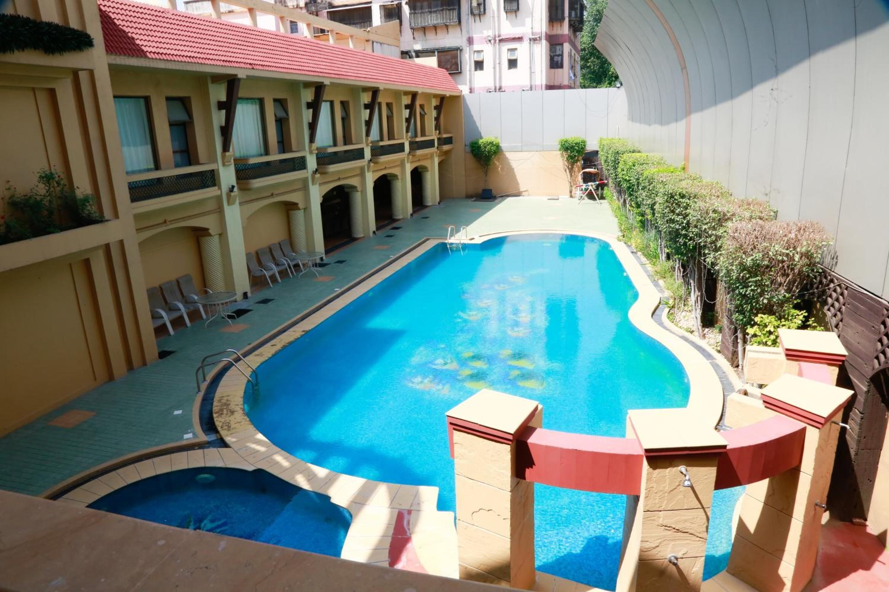 A swimming pool with a curved design, surrounded by lounge chairs and a covered area with a red roof.