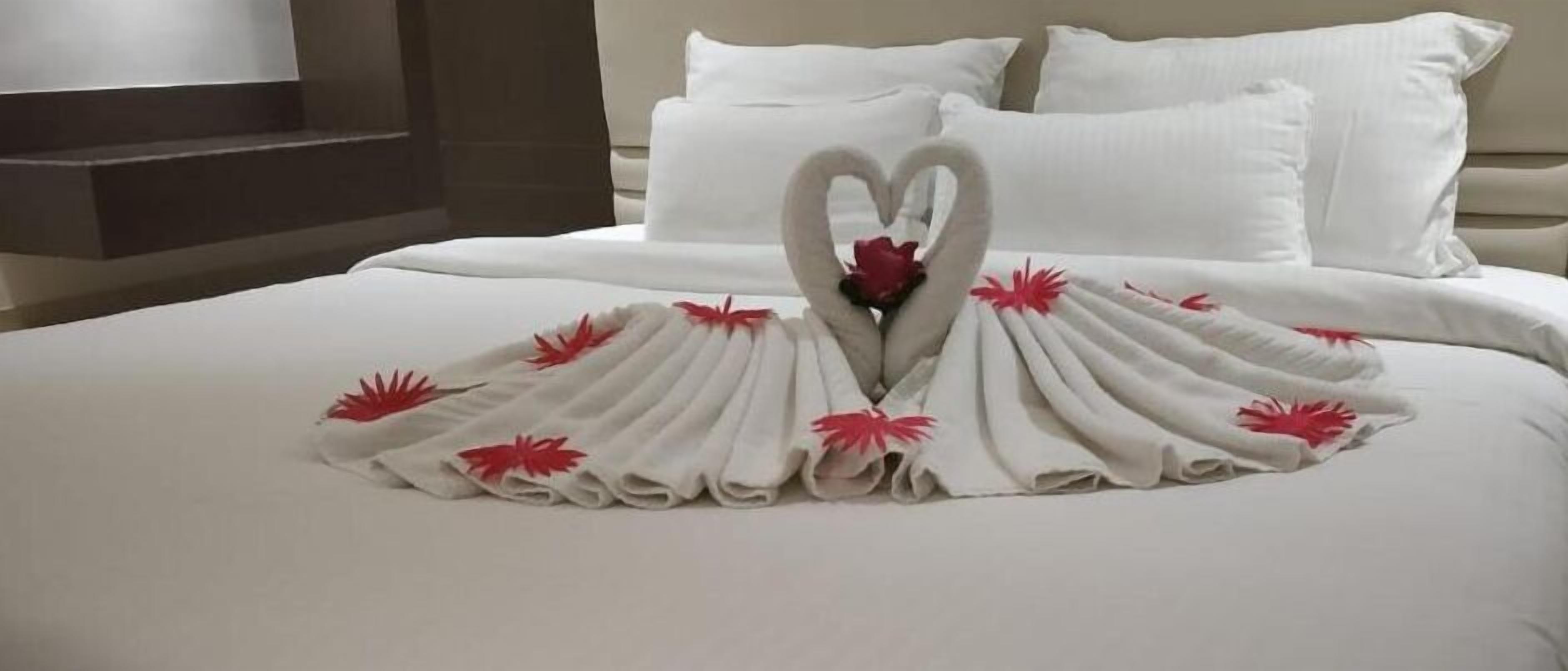 Una cama bien hecha con una decoración de toallas en forma de corazón y flores rojas.