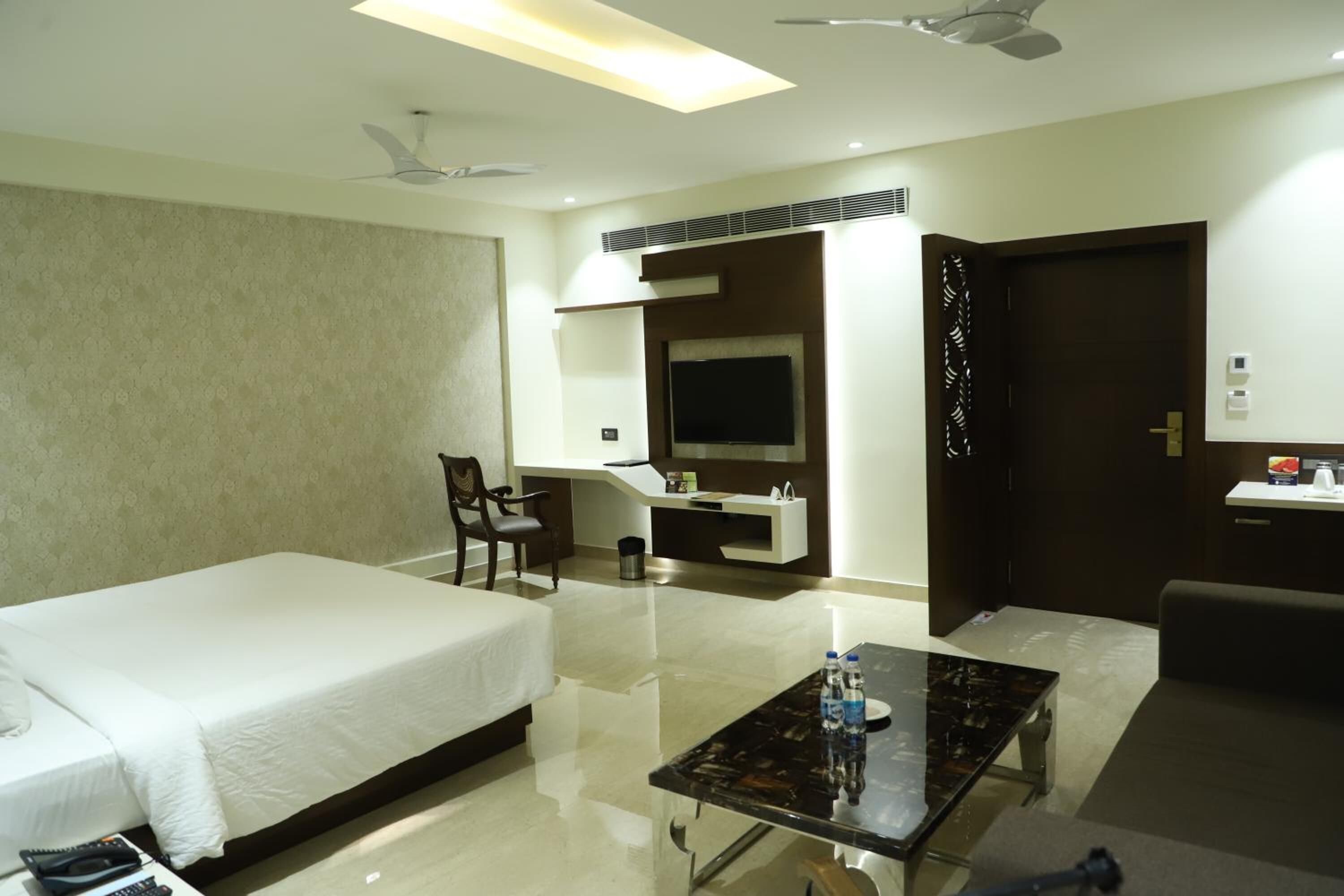 A hotel room with a bed, a desk, a chair, a TV, and a door.