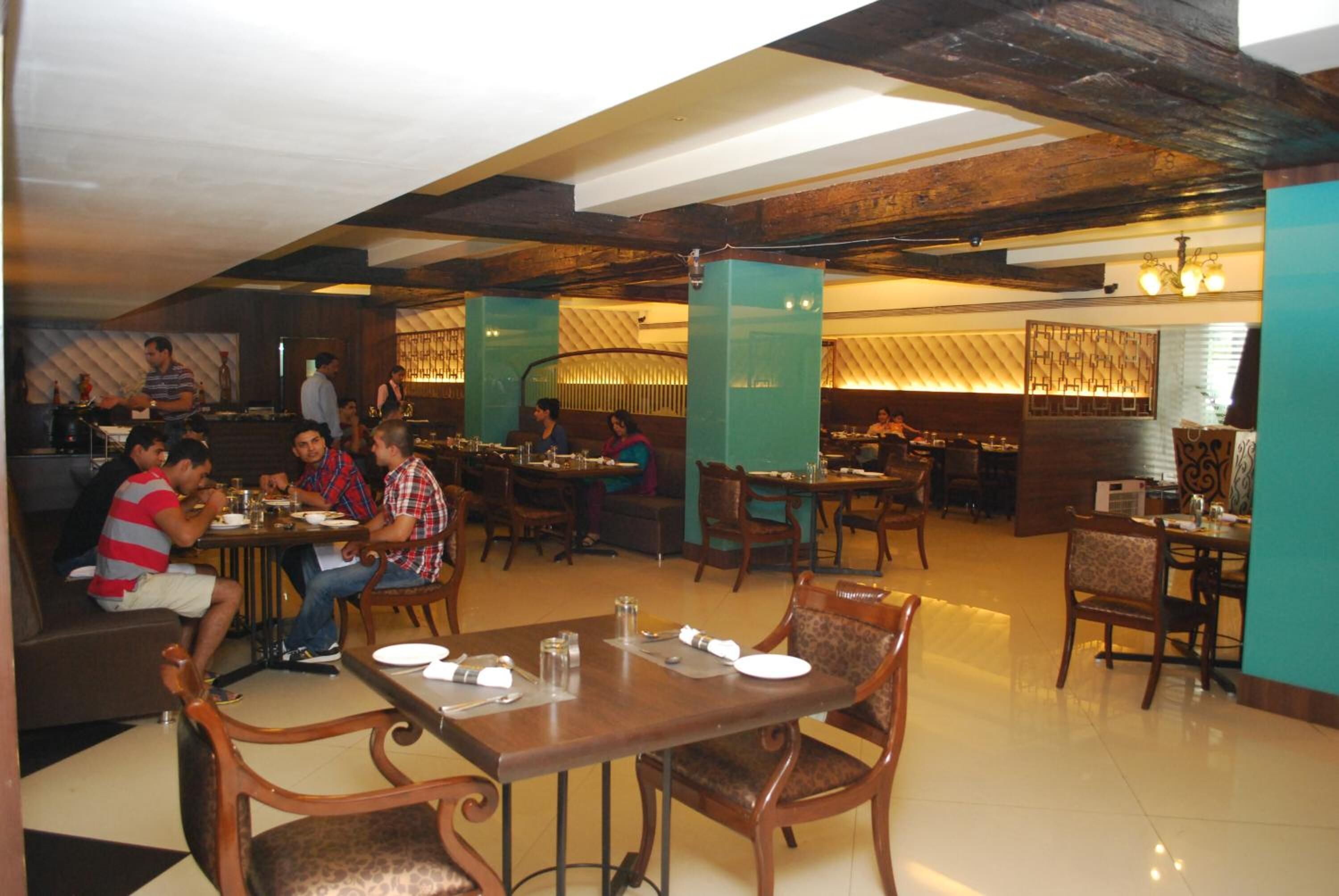Een restaurant met houten tafels en stoelen, een bar en een hoge ruimte met zichtbare balken.