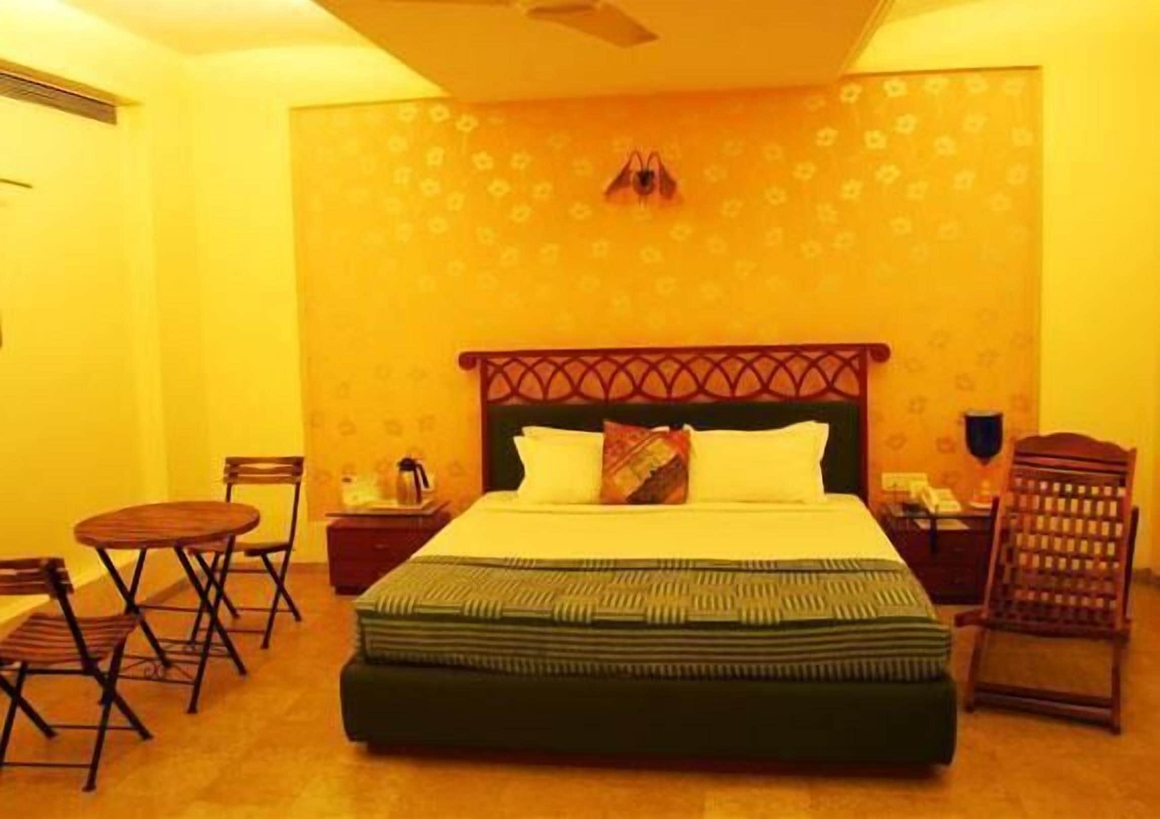 A hotel room with a large bed, a small table, two chairs, a nightstand, and a wall-mounted phone.