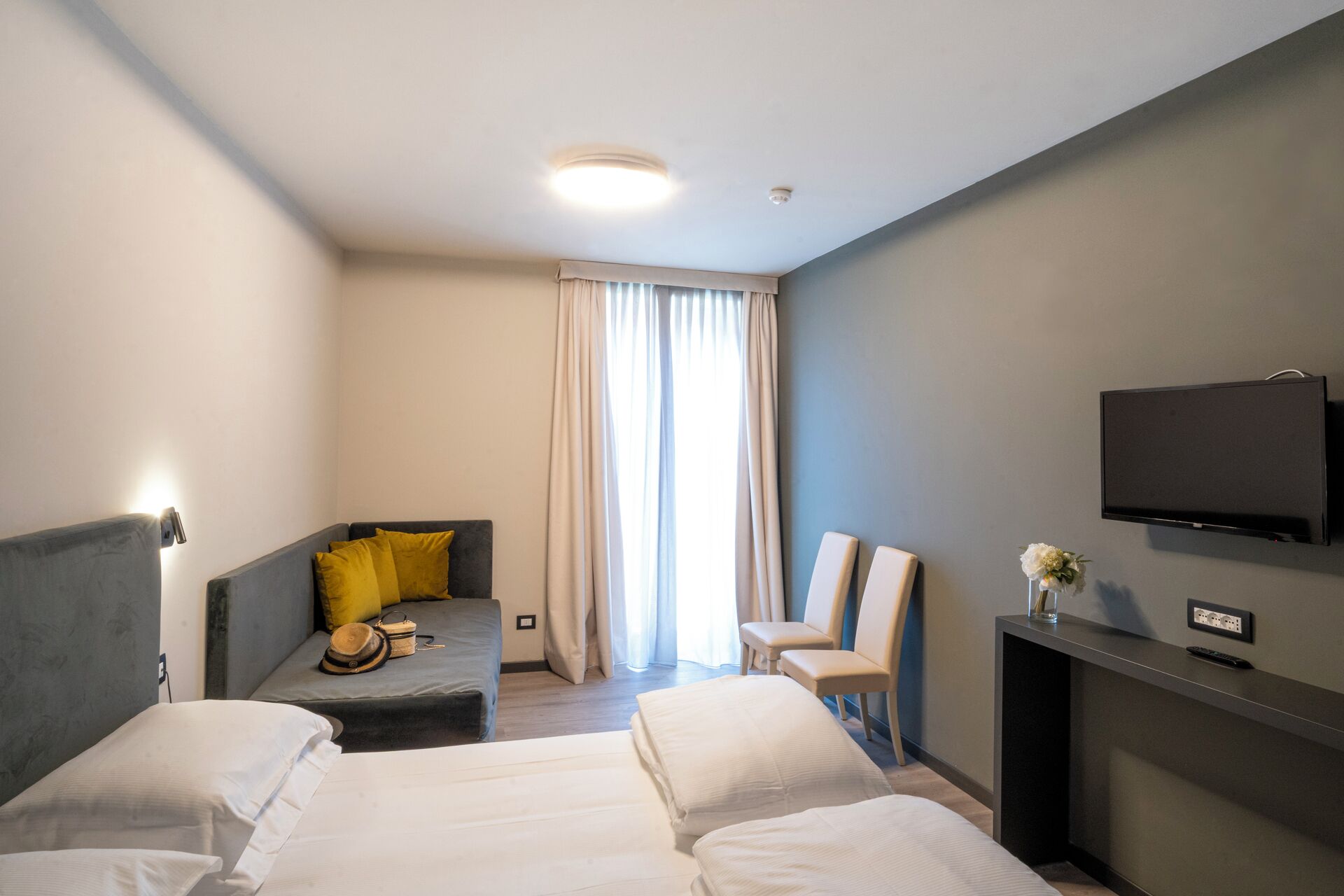 A hotel room with two beds, a sofa, a TV, and a desk with a vase of flowers.