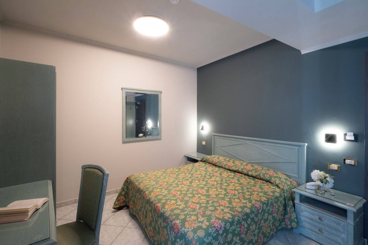 A bedroom with a bed, bedside table, mirror, and a dresser.