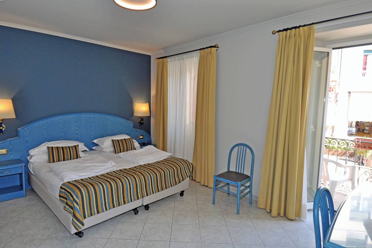 A hotel room with a large bed, two bedside tables, a chair, and a view of the outside.