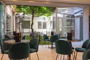 Un café moderno con mesas redondas y sillas verdes, una escalera en espiral y un árbol en el centro.