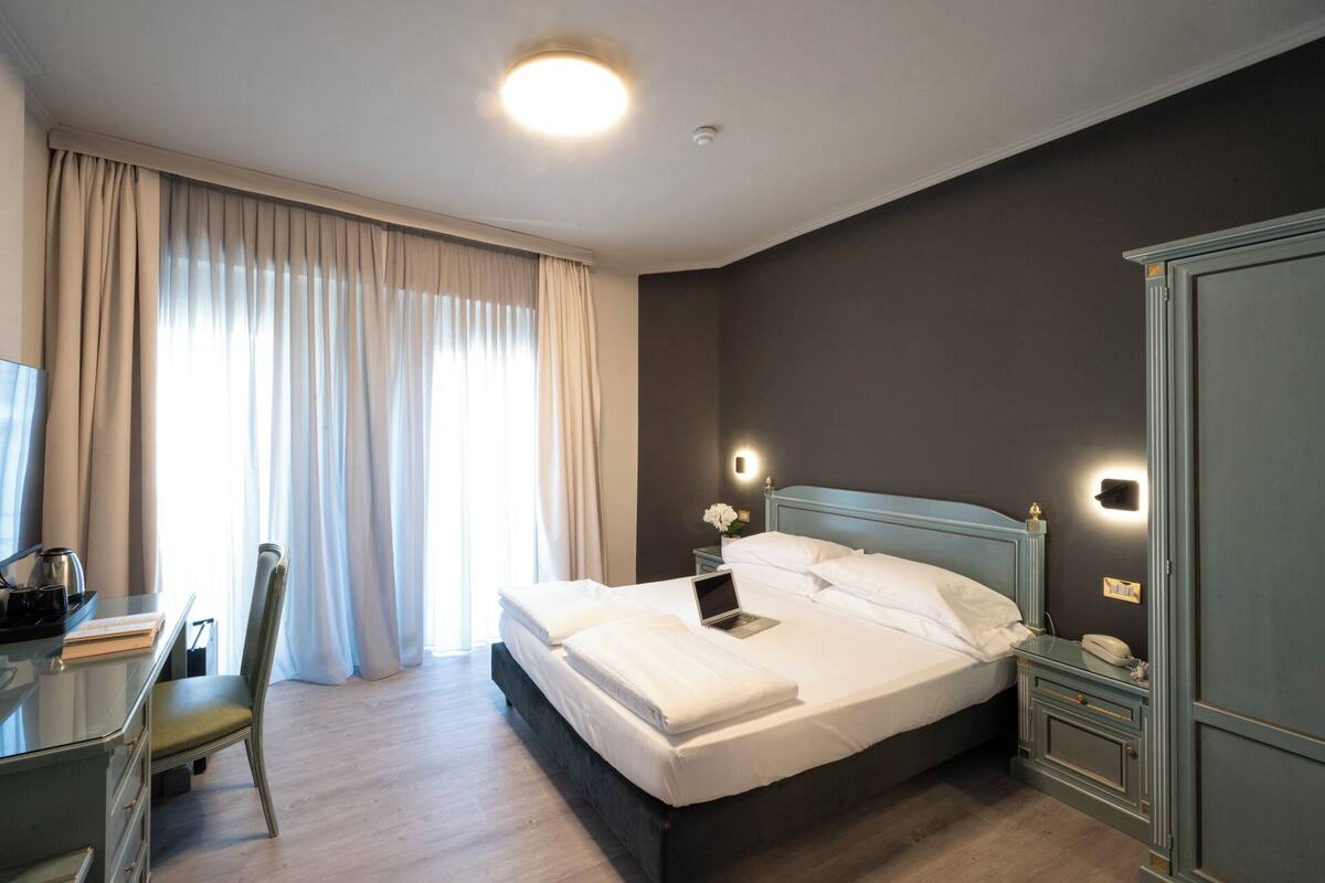A hotel room with a bed, a desk, a chair, and a wardrobe.