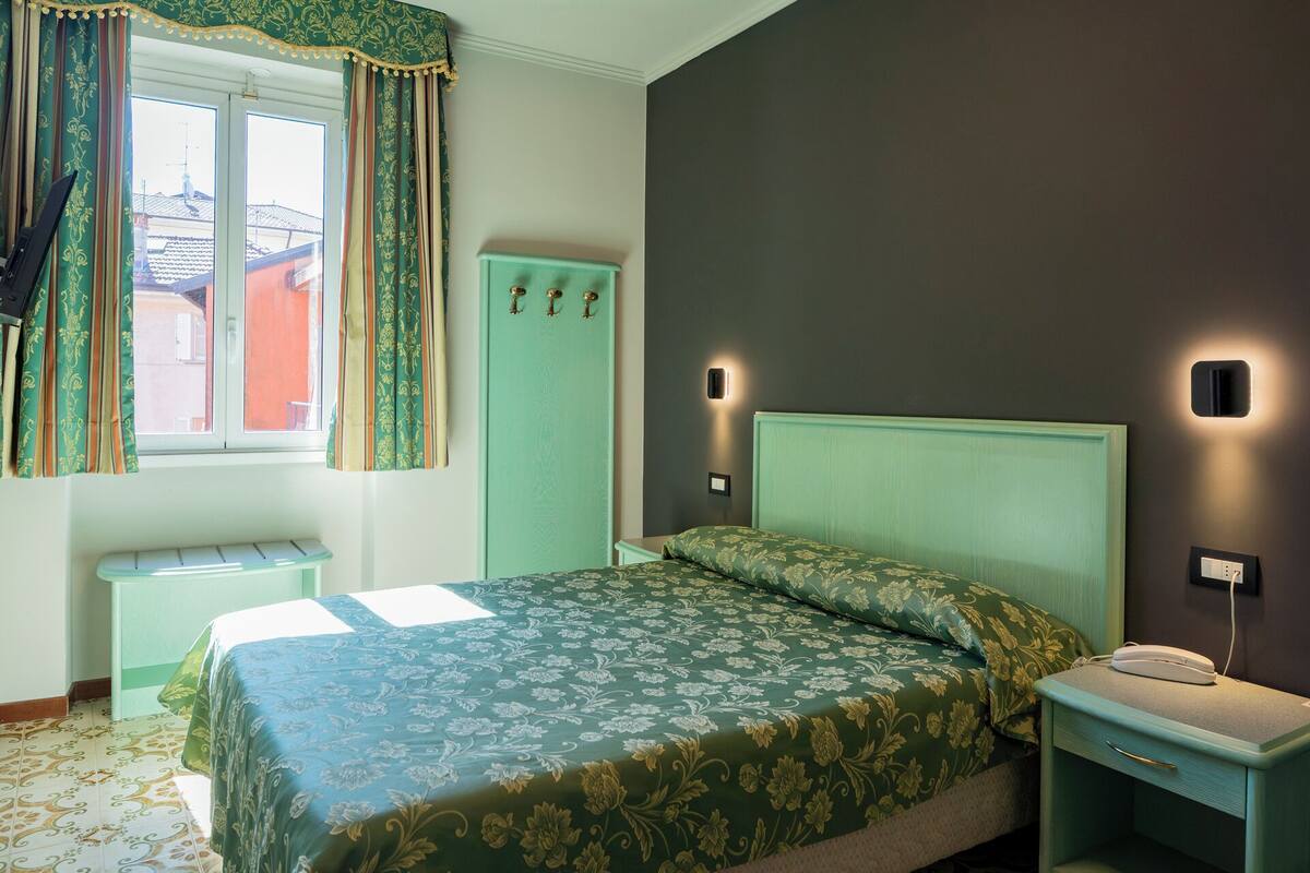 A bedroom with a bed, a nightstand, a wardrobe, and a window with curtains.