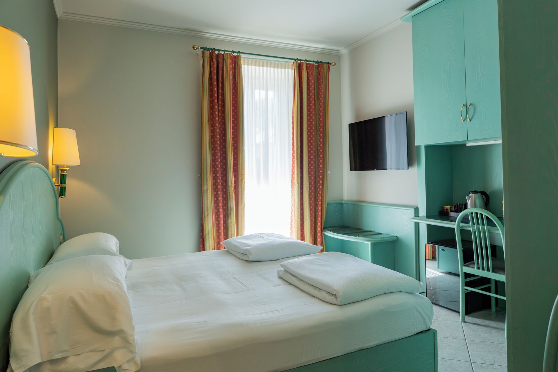 A hotel room with a bed, a desk, a chair, a TV, and a wardrobe.