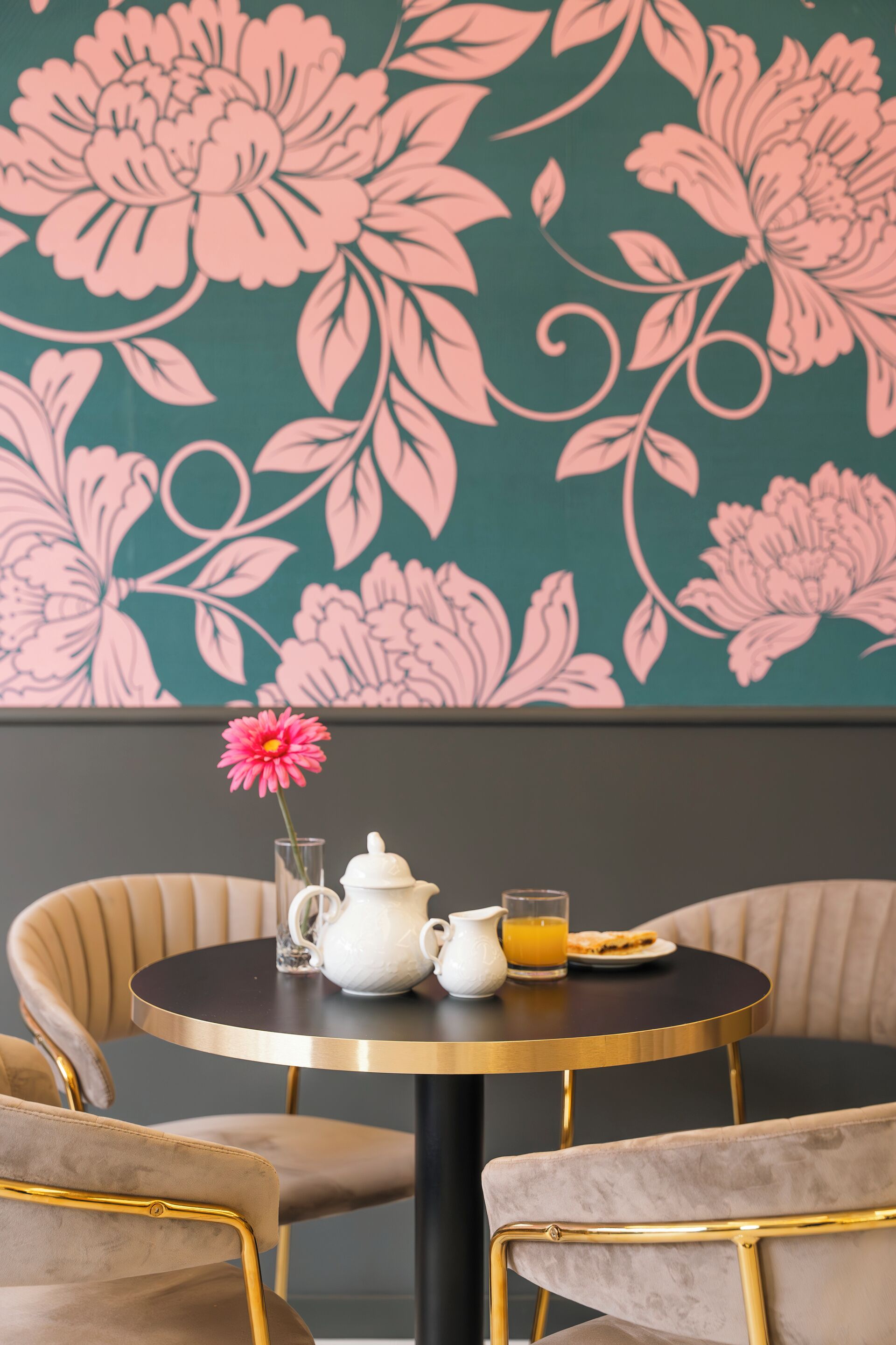 Ein Essbereich mit einem runden Tisch, zwei Stühlen, einer Vase mit einer rosa Blume, einer weißen Karaffe, einem Glas Orangensaft und einem Teller mit Essen.