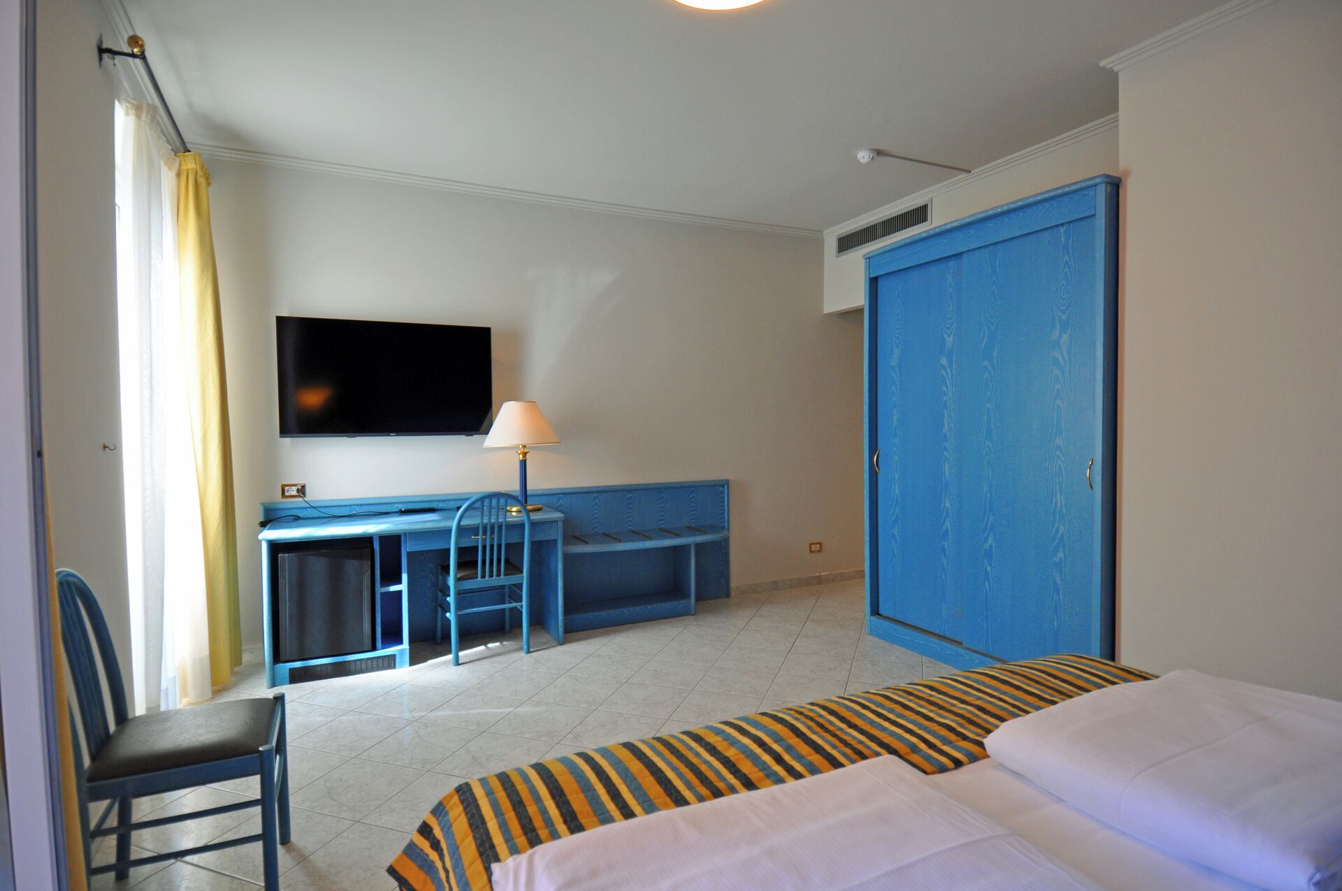 Ett hotellrum med en säng, ett skrivbord, en stol, en tv och en garderob.
