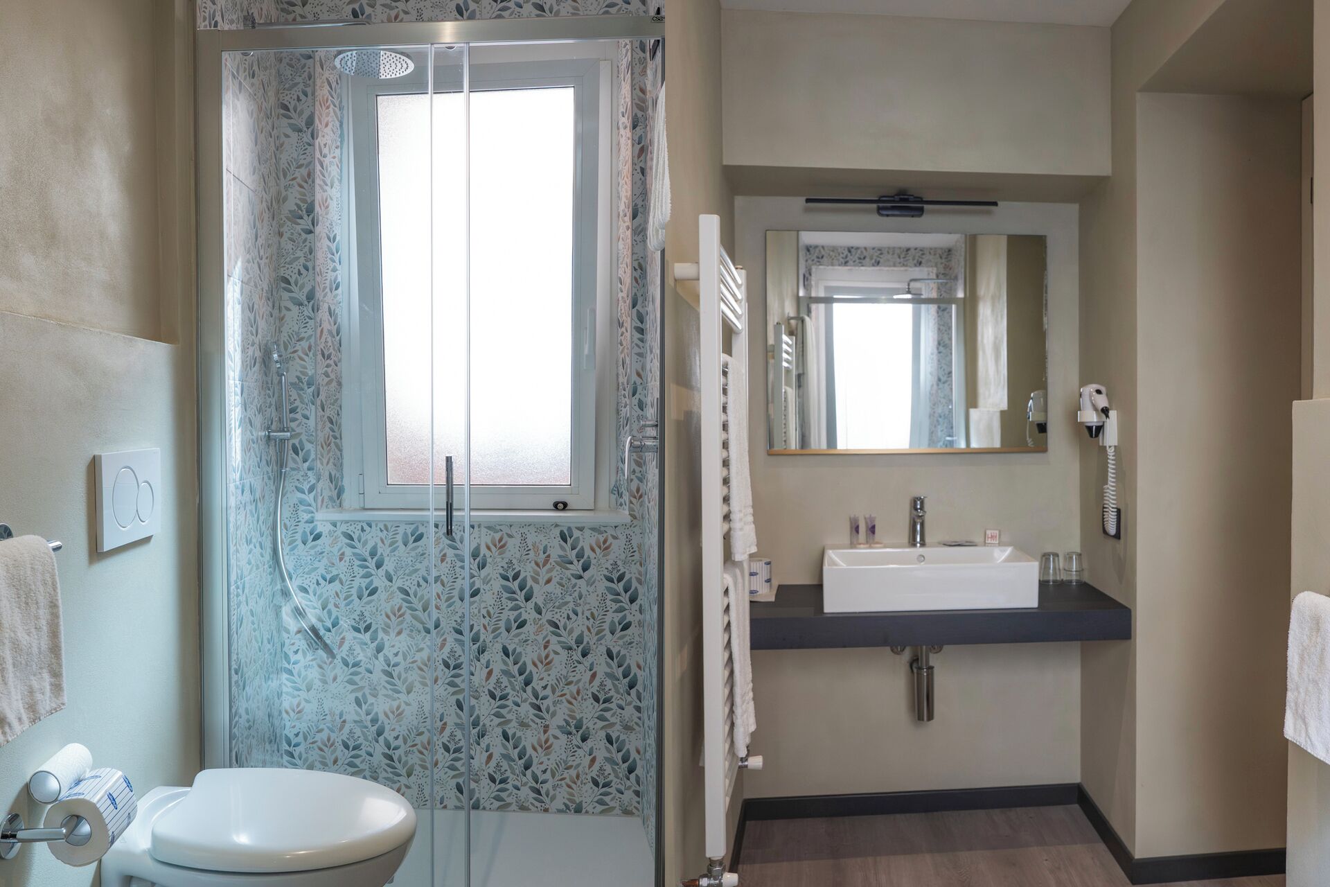 Un baño con inodoro, ducha con vidrio esmerilado, lavabo con espejo y perchero para toallas.