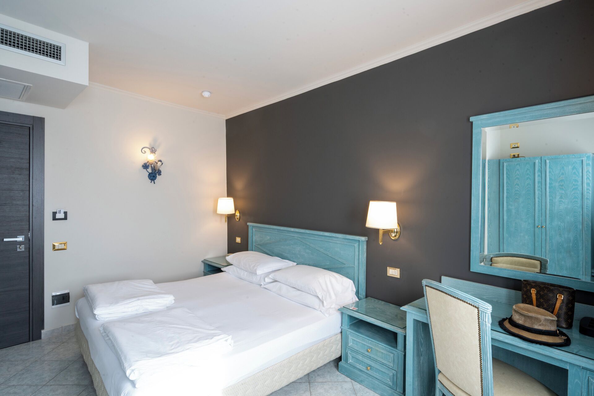 Ein Hotelzimmer mit einem Bett, Nachttischen, einem Schreibtisch, einem Sessel, einem Spiegel und einem Kleiderschrank.