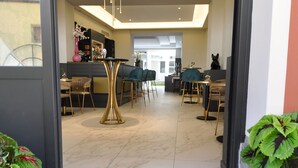 A hotel entrance with a black doormat reading "Carour 30 TRE" and a modern interior featuring a bar area with green chairs and a round ceiling light. - Cavour 30TRE - Hotel Moderno (Stresa)