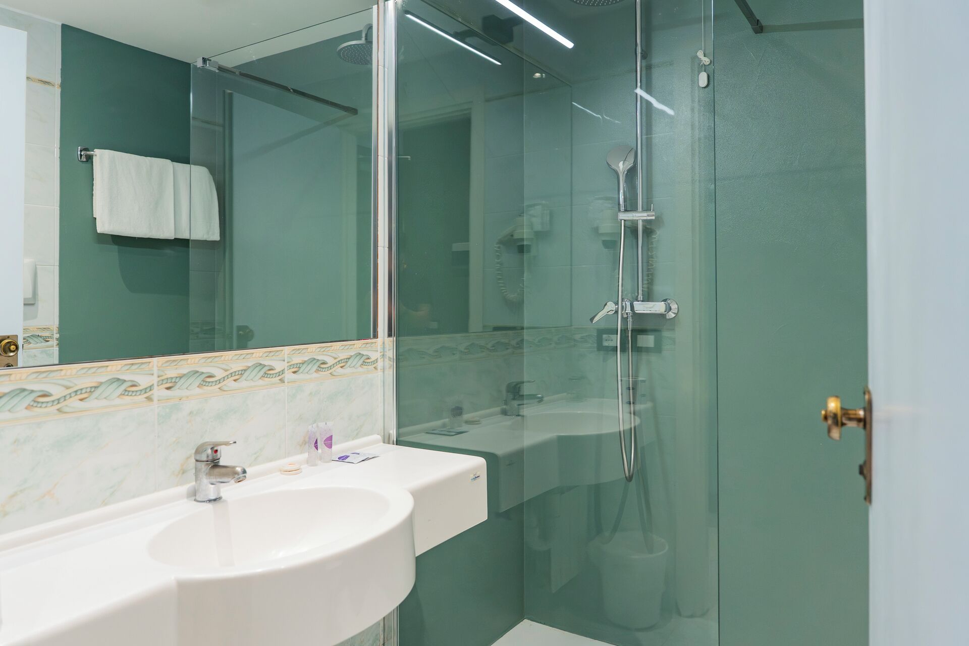 A modern bathroom with a glass-enclosed shower, a white sink, and a mirror with a decorative tile backsplash.