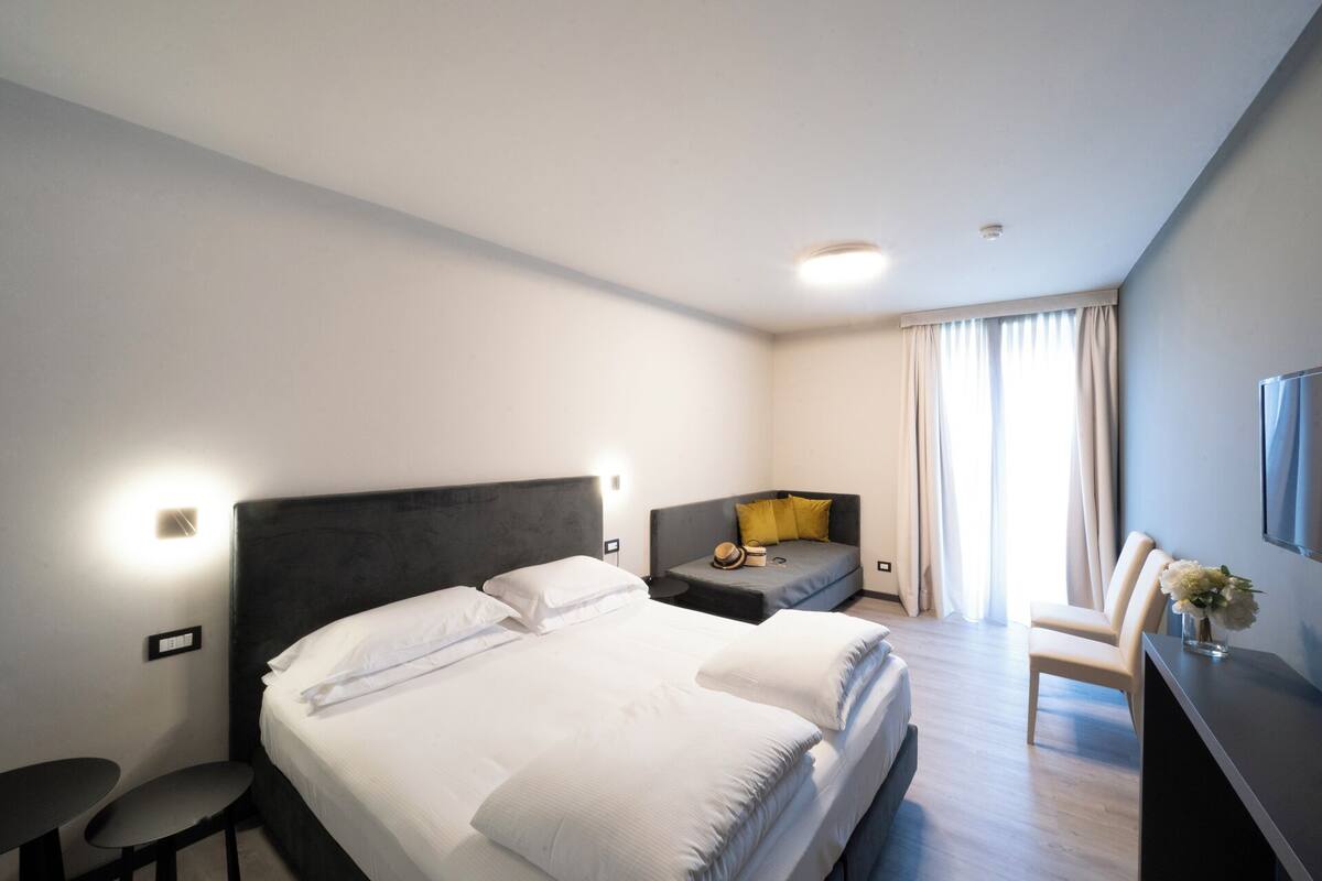 A modern hotel room with a large bed, a small sofa, a desk, and a TV.