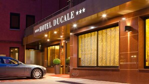 Een hotelentree met een bord waarop 'HOTEL DUCALE' staat en een auto ervoor geparkeerd.
