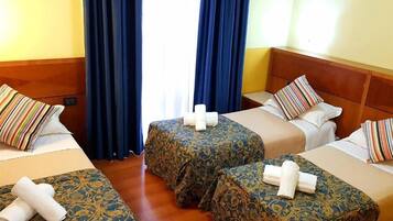 Habitación de hotel con dos camas individuales, cada una con una colcha estampada y una toalla enrollada. El suelo es de madera, el cabecero también, y hay una ventana con cortinas azules.