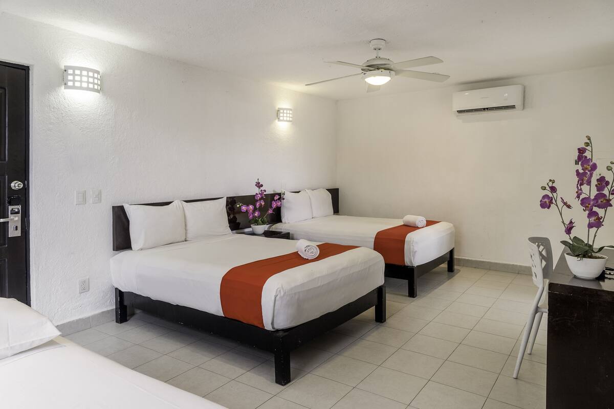 A hotel room with two beds, a ceiling fan, an air conditioner, and a desk with a chair.