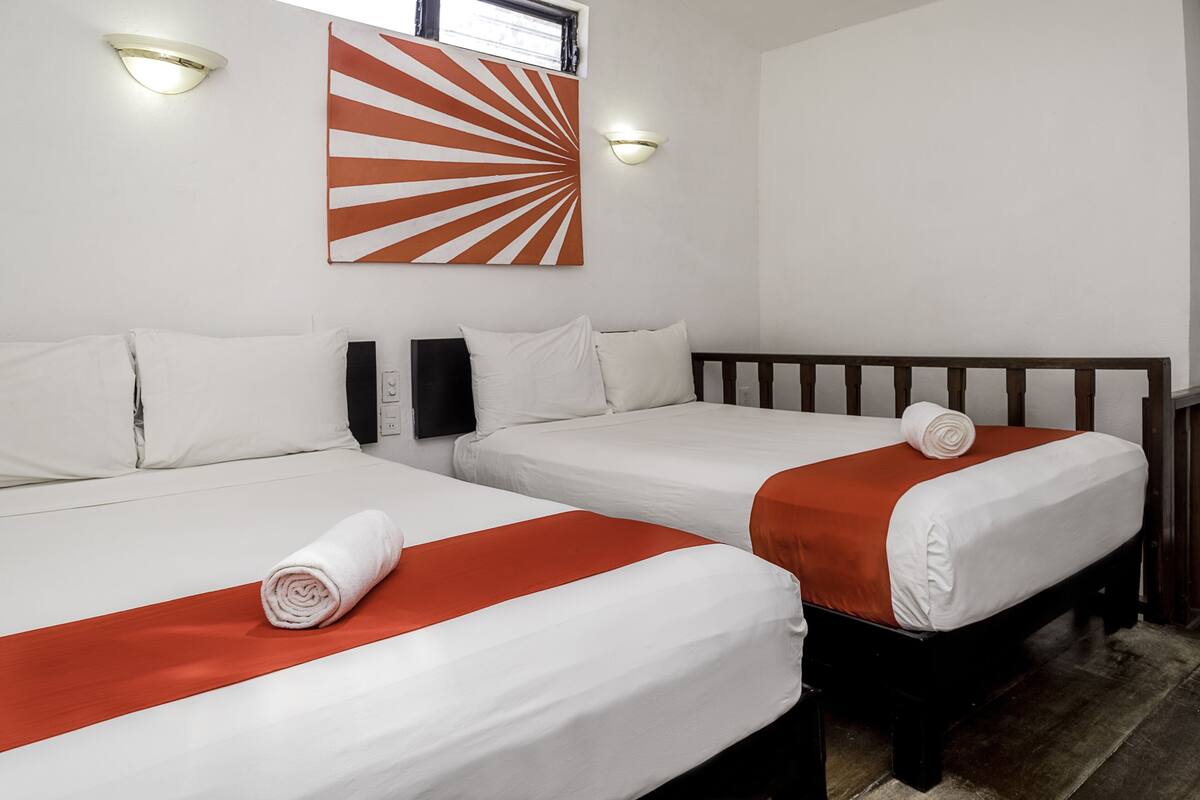 A hotel room with two beds, white linens, and orange bedspreads.