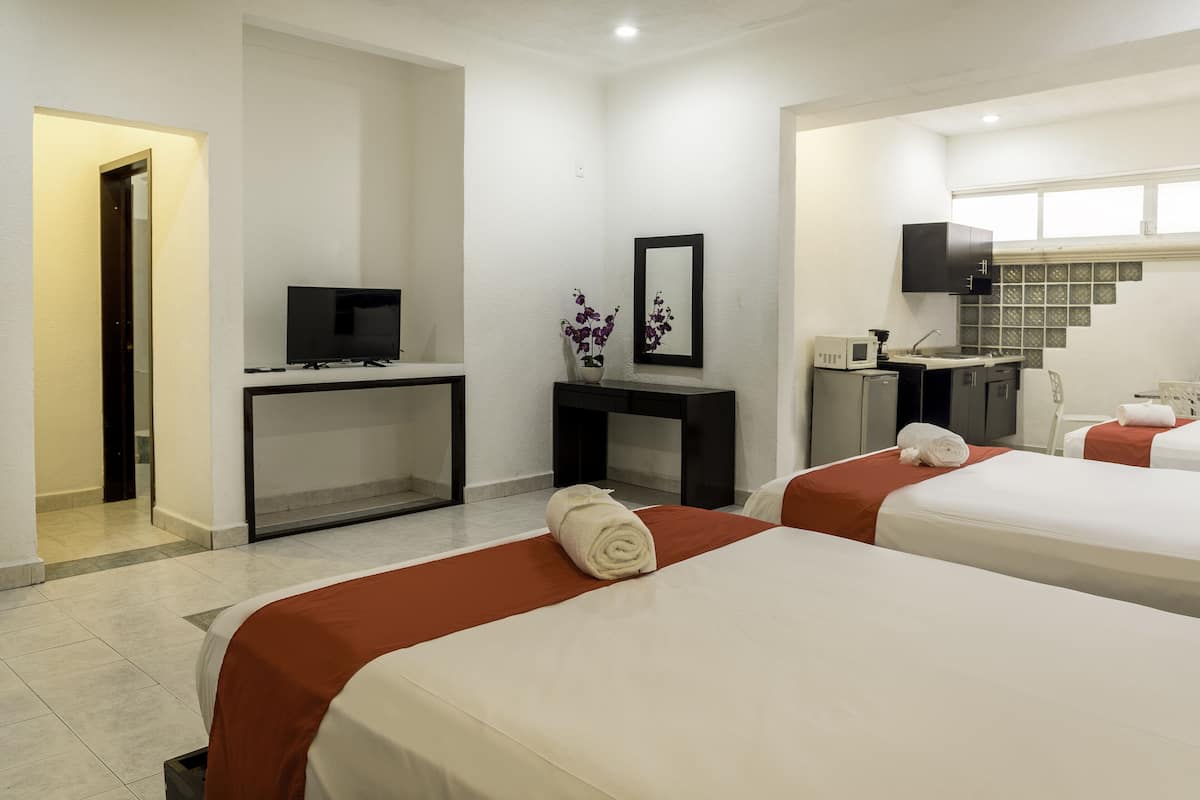 A hotel room with two beds, a desk with a TV, a small kitchen area, and a bathroom.