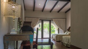 Ein Schlafzimmer mit Bett, Schreibtisch mit Lampe und Stuhl. Ein Fenster mit Vorhängen bietet Blick ins Grüne.