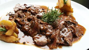 A plate of beef with mushrooms and potatoes, garnished with rosemary.